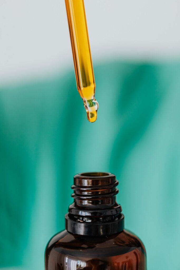 A glass dropper releasing a golden drop above an open amber bottle